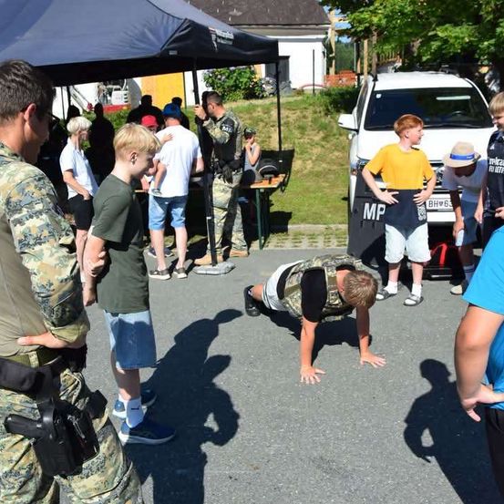 Eine Gruppe von Menschen, darunter ein Mann in Uniform, versammelt sich um einen Mann, der auf der Straße Liegestütze macht.