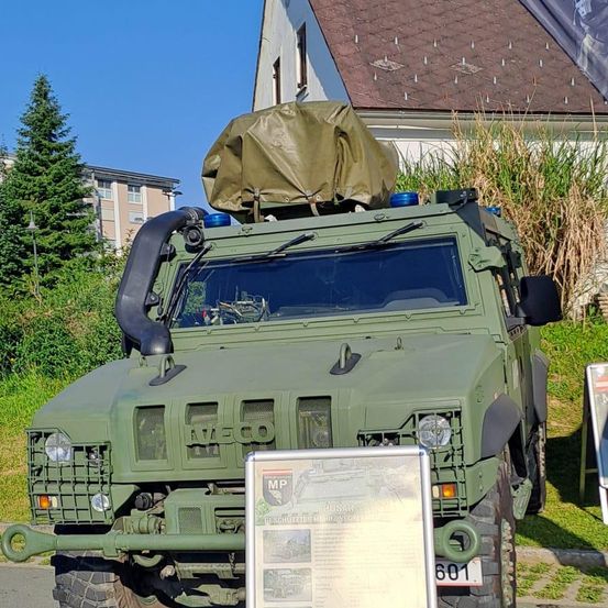 Ein grünes Militärfahrzeug mit einer Plane oben ist auf dem Rasen vor einem Haus geparkt.