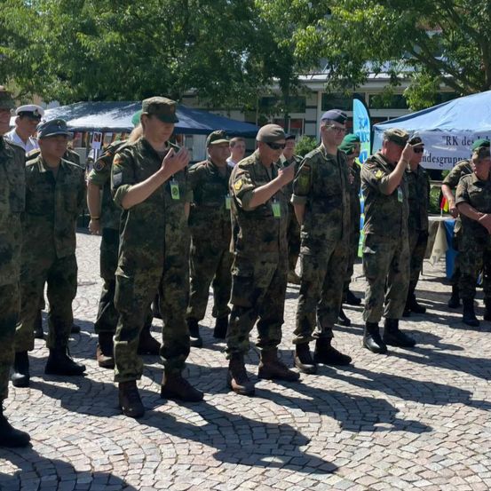 Eine Gruppe von Militärangehörigen in Tarnuniformen steht in einer Reihe, möglicherweise an einer Zeremonie oder Veranstaltung teilnehmend.