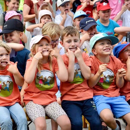 Eine Gruppe von Kindern in passenden orangefarbenen T-Shirts mit Cartoon-Charakteren sitzt auf einer Bank, lächelt und posiert für ein Foto.