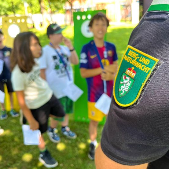 Eine Gruppe von Kindern in einem Park mit einer Person, die einen Berg-und Naturwacht-Patch auf ihrer Uniform trägt.