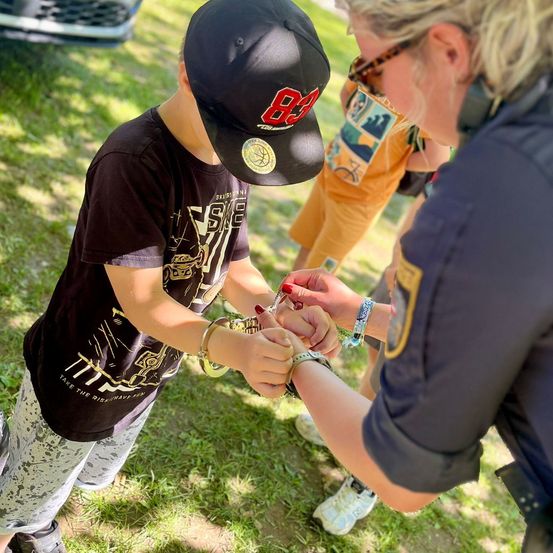 Ein junger Junge mit schwarzem Hut und Shirt wird von einer Polizistin mit Handschellen gezeigt.