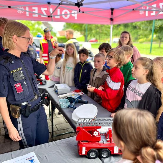 Eine Polizistin demonstriert ein Spielzeug-Feuerwehrauto einer Gruppe von Kindern unter einem Zelt.