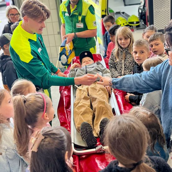 Eine Gruppe von Kindern beobachtet, wie ein Sanitäter demonstriert, wie man eine Trage benutzt.