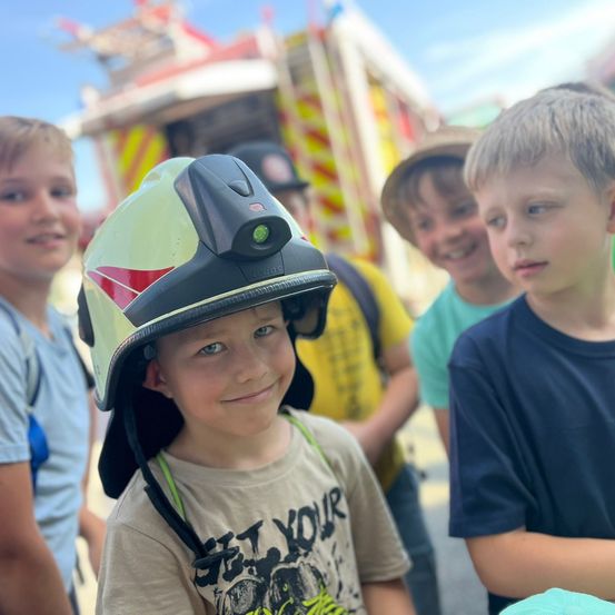 Eine Gruppe von Jungen, einer trägt einen Feuerwehrhelm, steht vor einer Karussellfahrt.