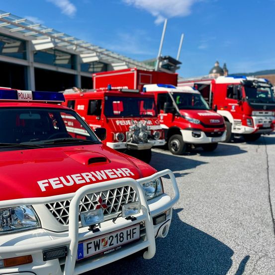 Eine Reihe roter Feuerwehrfahrzeuge mit dem Wort Feuerwehr auf der Vorderseite des nächsten, auf einem Parkplatz geparkt.