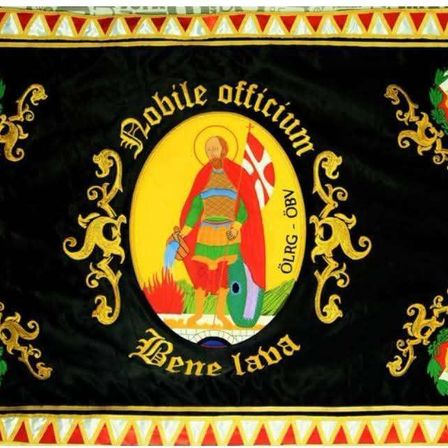 Ein schwarzer Banner mit einem goldenen Emblem, das eine Figur mit Schild und Schwert zeigt, umgeben von dekorativen Elementen und lateinischem Text.