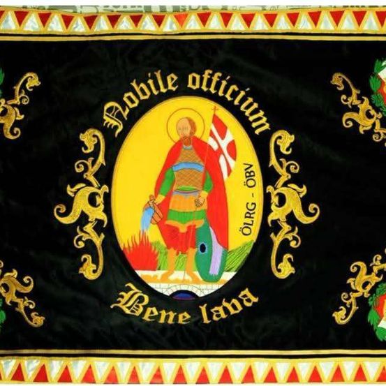 Ein schwarzer Banner mit einem goldenen Emblem, das eine Figur mit Schild und Schwert zeigt, umgeben von dekorativen Elementen und lateinischem Text.