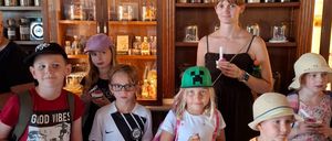 A group of children and a woman stand in front of a shelf filled with labeled jars, each holding a small cup of ice cream.