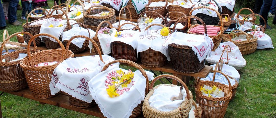 Eine Reihe von Weidenkörben, gefüllt mit bestickten Tüchern und gelben Blumen, auf einem Holztisch im Freien.