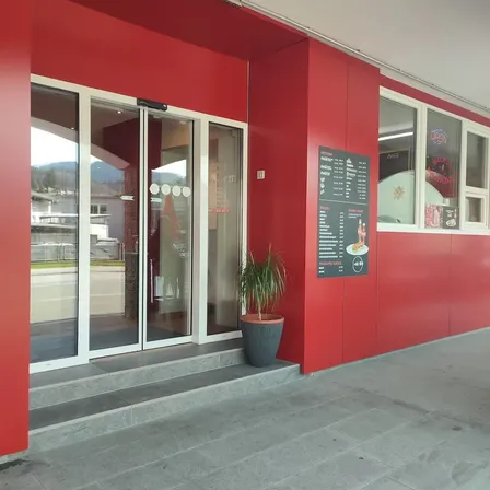 Ein rotes Gebäudeaußen mit Glastüren und Fenstern, einem Menübrett und einem Topf mit Pflanzen auf der rechten Seite.