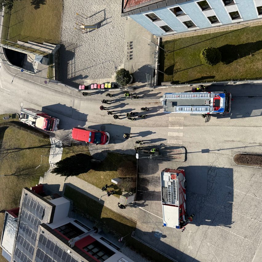 Eine Luftaufnahme von Rettungskräften, die auf einen Vorfall in einer Kleinstadt reagieren, mit Feuerwehrwagen und Personal rund um ein Gebäude stationiert.