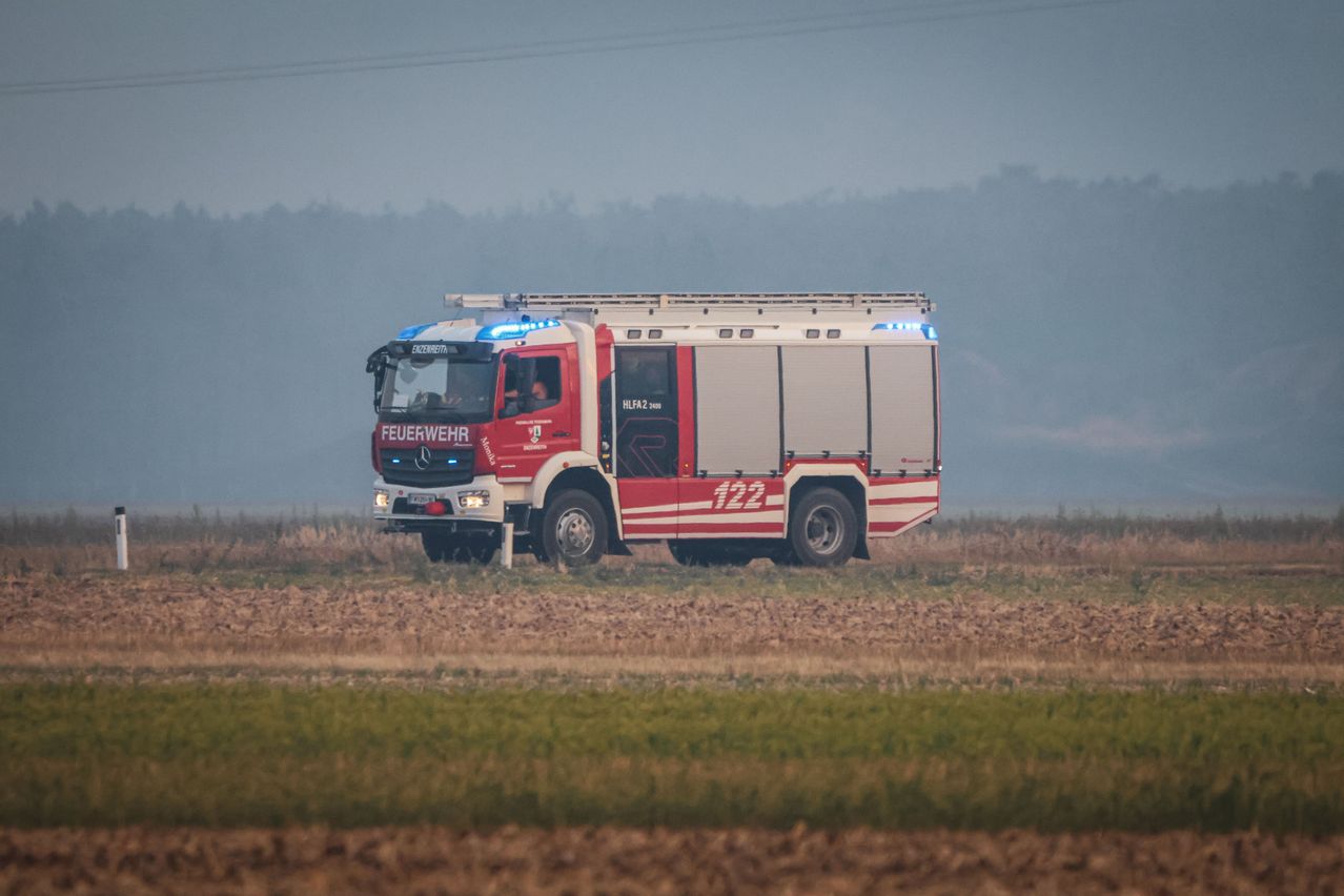 Ein roter und weißer Feuerwehrwagen mit der Nummer 122 auf der Seite steht auf einem Feld mit Nebel im Hintergrund.