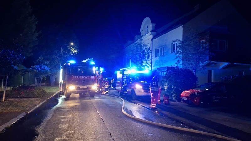 Feuerwehrleute reagieren nachts auf einen Notfall auf einer Straße mit Gebäuden und geparkten Autos.