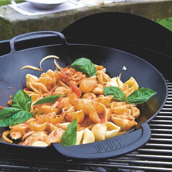 Eine Weber Gusseisenpfanne auf einem Grill mit Nudeln, Gemüse und Basilikumblättern.