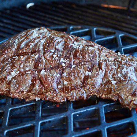 Ein Steak wird auf einem Grill mit einem charakteristischen Muster gegrillt, mit Salz bestreut und zeigt Anzeichen von Garung.