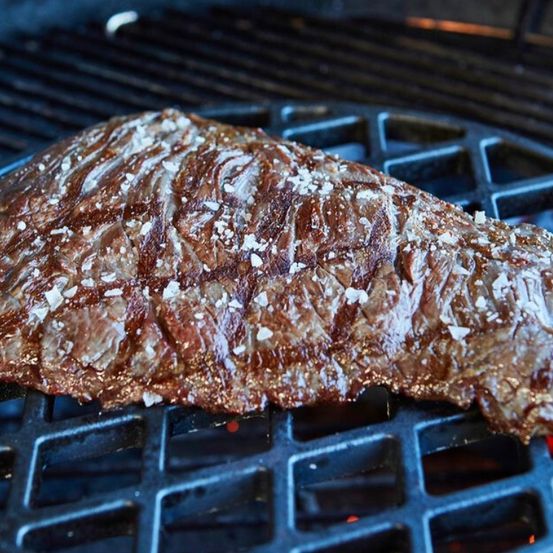 Ein Steak wird auf einem Grill mit einem charakteristischen Muster gegrillt, mit Salz bestreut und zeigt Anzeichen von Garung.