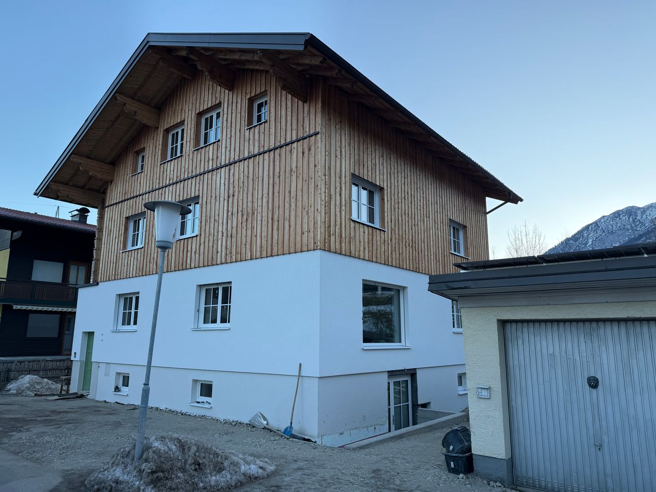 Ein modernes Gebäude mit Holzverkleidung und weißen Wänden. Es hat mehrere Fenster und einen Laternenpfahl davor. In der Nähe befinden sich einige Reinigungsutensilien und ein Mülleimer.