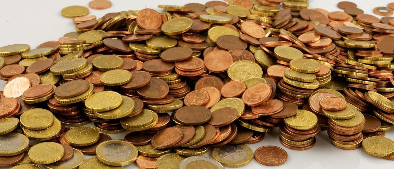 Ein Haufen gemischter Euro-Münzen auf einer weißen Oberfläche enthält Ein-, Zwei- und Fünf-Euro-Münzen.