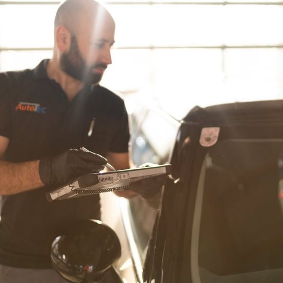Ein Mann in einem schwarzen Shirt mit 'AutoEC', der Handschuhe trägt, arbeitet mit einem Laptop an einem Auto.