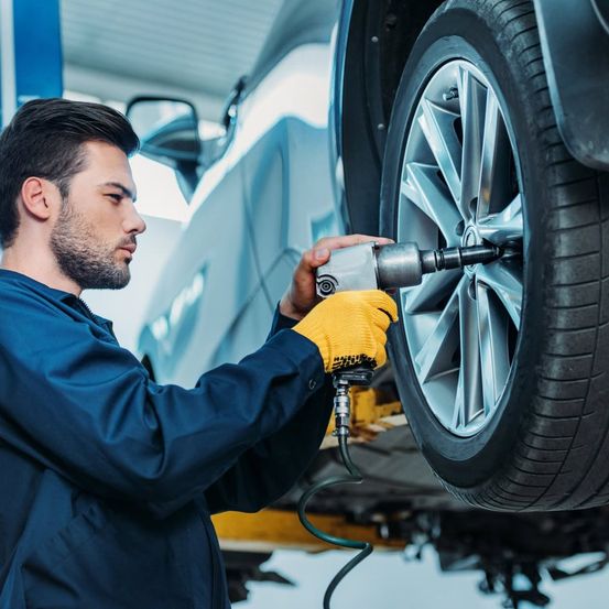 Ein Mann in einer blauen Uniform und gelben Handschuhen benutzt ein Werkzeug, um die Radmuttern eines Autos festzuziehen.