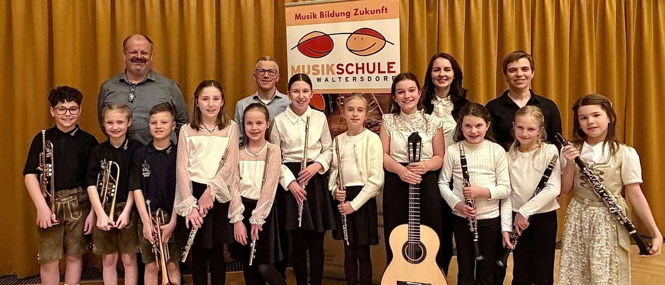 Eine Gruppe von Kindern und Erwachsenen steht zusammen mit Musikinstrumenten vor einem Schild, das Musikschule Waltersdorre besagt.
