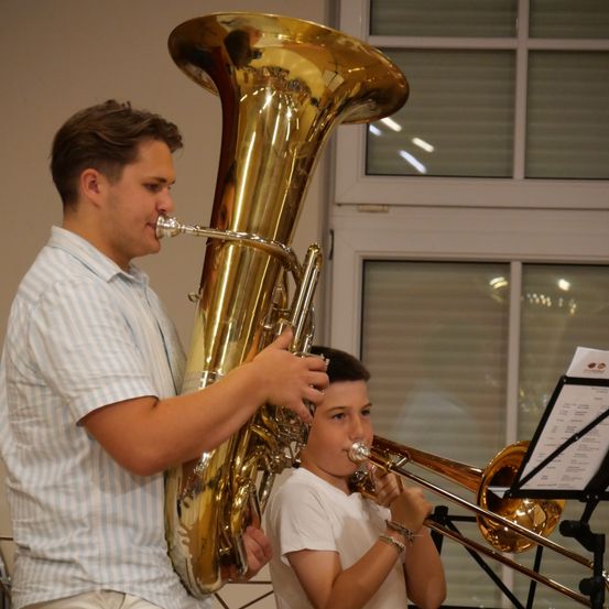 Ein junger Mann spielt Tuba, während ein anderer Junge Posaune spielt. Sie konzentrieren sich beide auf ihre Instrumente.
