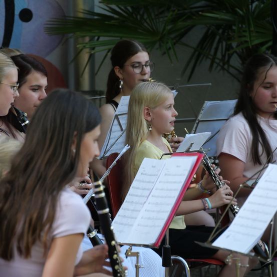 Eine Gruppe junger Mädchen spielt Musikinstrumente, darunter Klarinetten, während sie auf Stühlen sitzen und ihre Notenblätter betrachten.