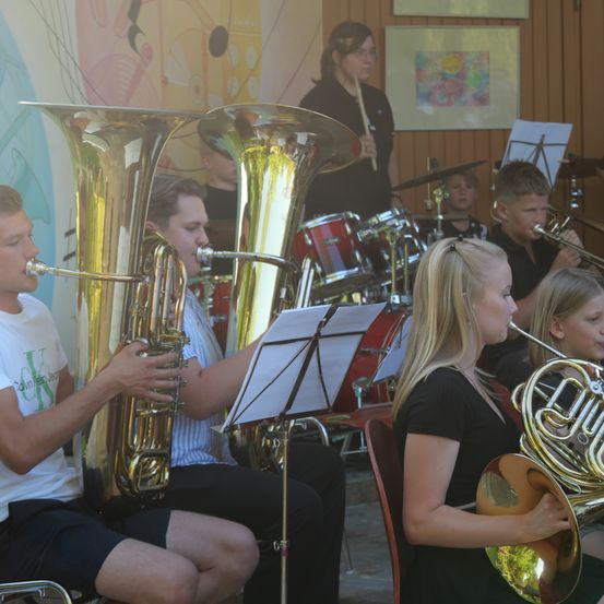 Eine Gruppe junger Musiker spielt Blechblasinstrumente, darunter Tubas und Hörner, in einem Raum mit farbenfrohen Wänden und Musikinstrumenten.