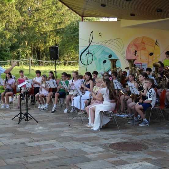 Eine Schulband übt im Freien unter einem Pavillon, wobei Schüler verschiedene Instrumente wie Trompeten und Klarinetten spielen, während ein Lehrer dirigiert.