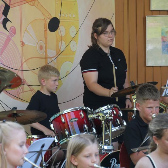 Eine Gruppe von Kindern und Jugendlichen spielt Musikinstrumente in einem Raum mit einer farbenfrohen Wand im Hintergrund.
