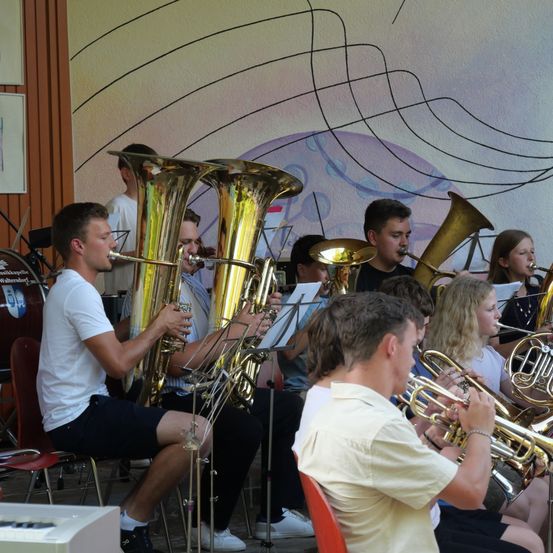 Eine Gruppe von Musikern spielt Blechblasinstrumente in einem Raum mit einer farbenfrohen Wand im Hintergrund.