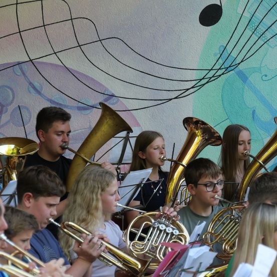 Eine Gruppe von Kindern und Jugendlichen spielt Blechblasinstrumente in einer Band, mit einem farbenfrohen musikalischen Hintergrund.
