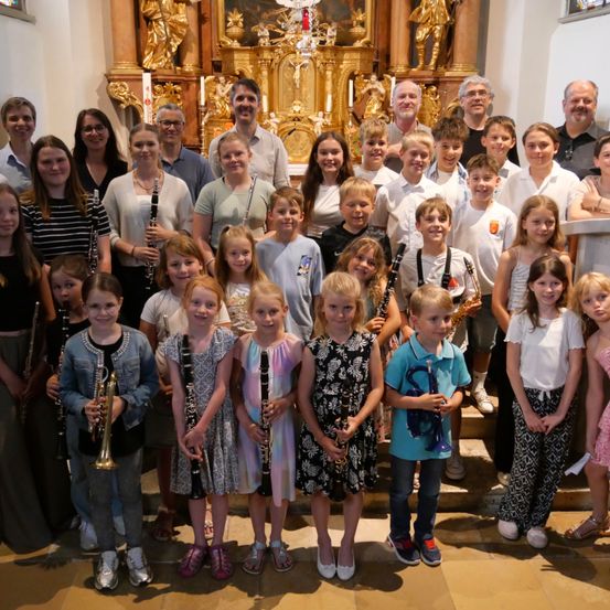 Eine Gruppe von Kindern und Erwachsenen, alle mit Musikinstrumenten, posiert für ein Foto vor einem Kirchenaltar.