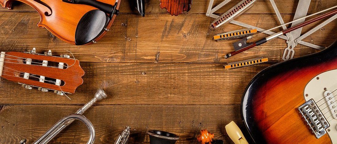 Eine Auswahl an Musikinstrumenten auf einer Holzoberfläche: Violine, Gitarre, Trompete, Mundharmonika, Flöte und andere. Jedes Instrument ist kunstvoll platziert.
