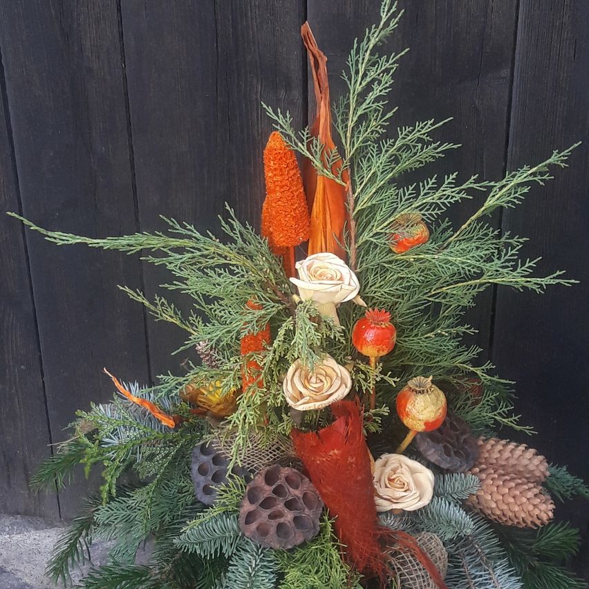 Eine lebhafte Blumenarrangement mit weißen Rosen, grünem Laub, orangefarbenen Akzenten und Tannenzapfen. Vor einem dunklen Holzhintergrund fügt es einen Hauch von Naturschönheit hinzu.