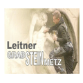 Ein Mann in einer Jacke schnitzert eine Skulptur einer liegenden Figur, mit einem Bier in der Hand. Das Bild hat einen Textüberlagerung, 'Leitner GRAB STEINMETZ'.