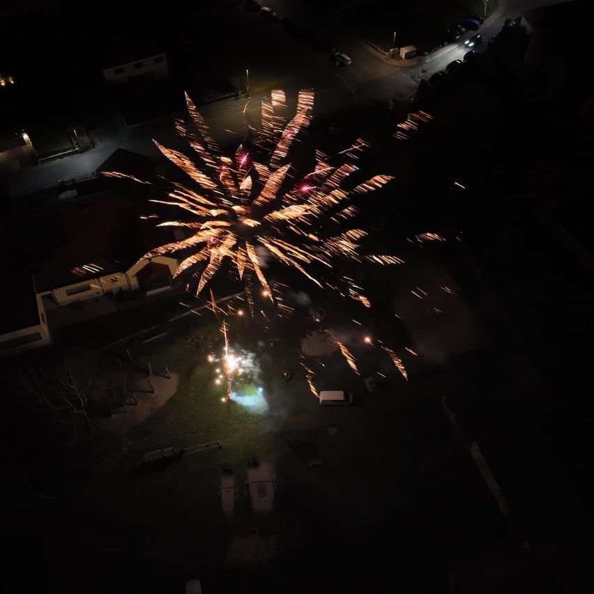 Ein Nachtluftbild zeigt ein lebhaftes Feuerwerk, das in der Nacht explodiert und die dunkle Umgebung mit farbenfrohen Funken beleuchtet.