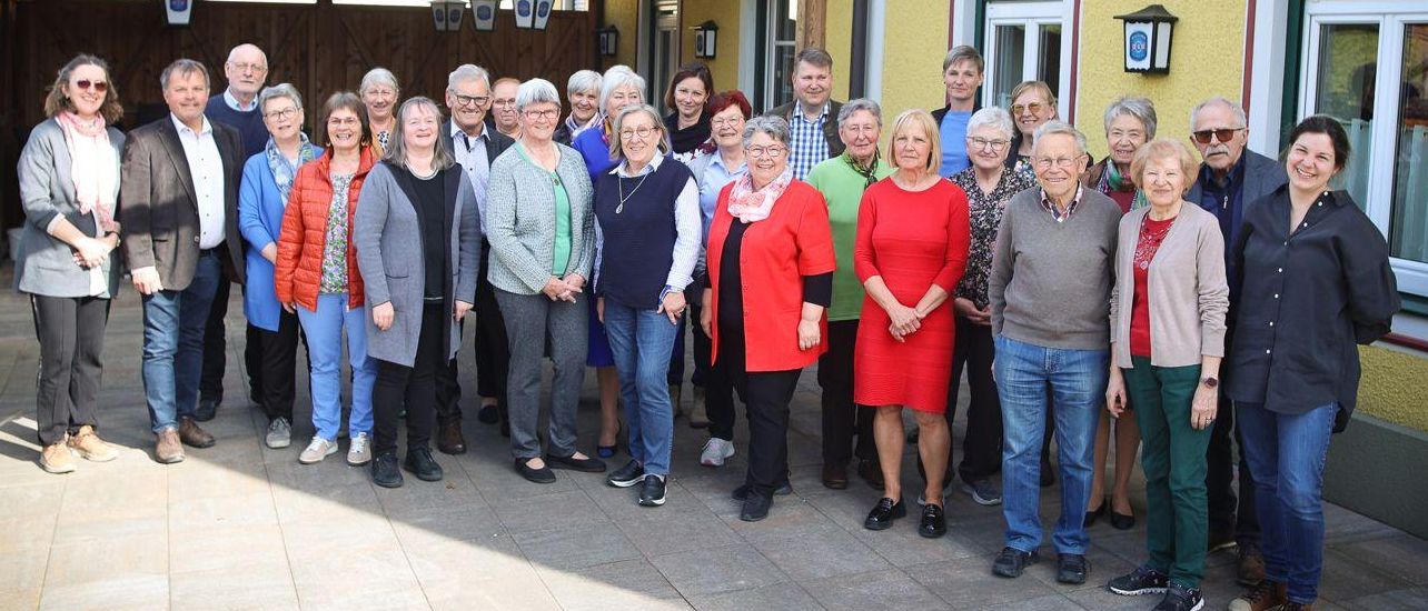 Eine Gruppe von Erwachsenen steht vor einem gelben Gebäude mit überdachter Veranda. Sie lächeln und posieren für ein Foto.