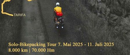 Ein Radfahrer fährt auf einem felsigen Pfad zwischen zwei großen Felswänden mit einer gelben Linie. Der Weg führt nach Tarifa, und das Wort 'Nordkap' steht in der oberen linken Ecke. Der Himmel ist bewölkt.