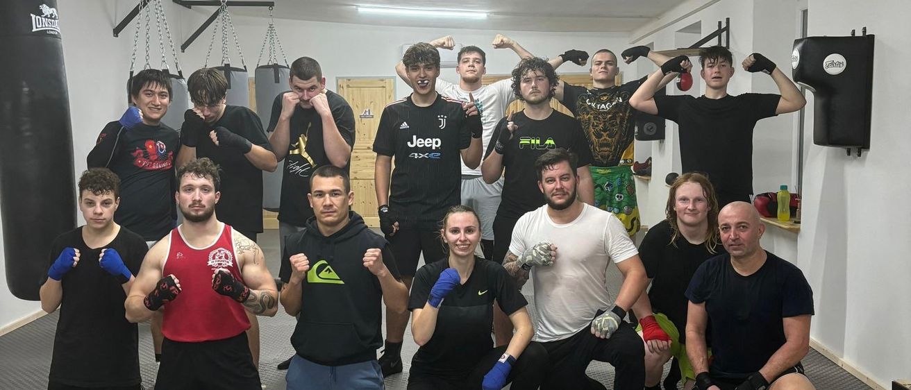 Eine Gruppe junger Menschen in einem Fitnessstudio posiert für ein Foto, alle in verschiedenen Sportbekleidungen und Boxhandschuhen.