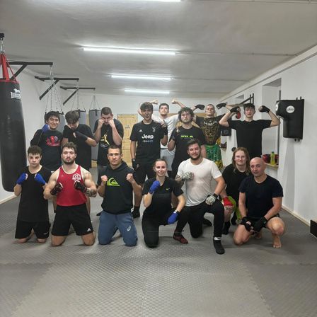 Eine Gruppe junger Boxer in schwarzen und roten Outfits mit Boxhandschuhen in einem Fitnessstudio mit Boxsäcken und Trainingsgeräten.