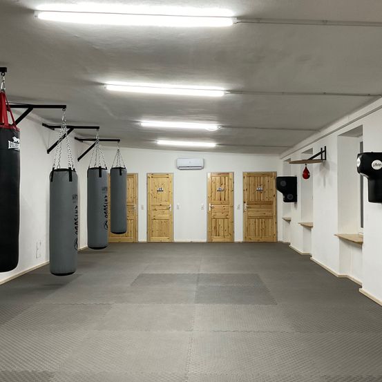 Ein leerer Raum mit Boxsäcken, die an der Decke hängen, und Holztüren an der Wand.