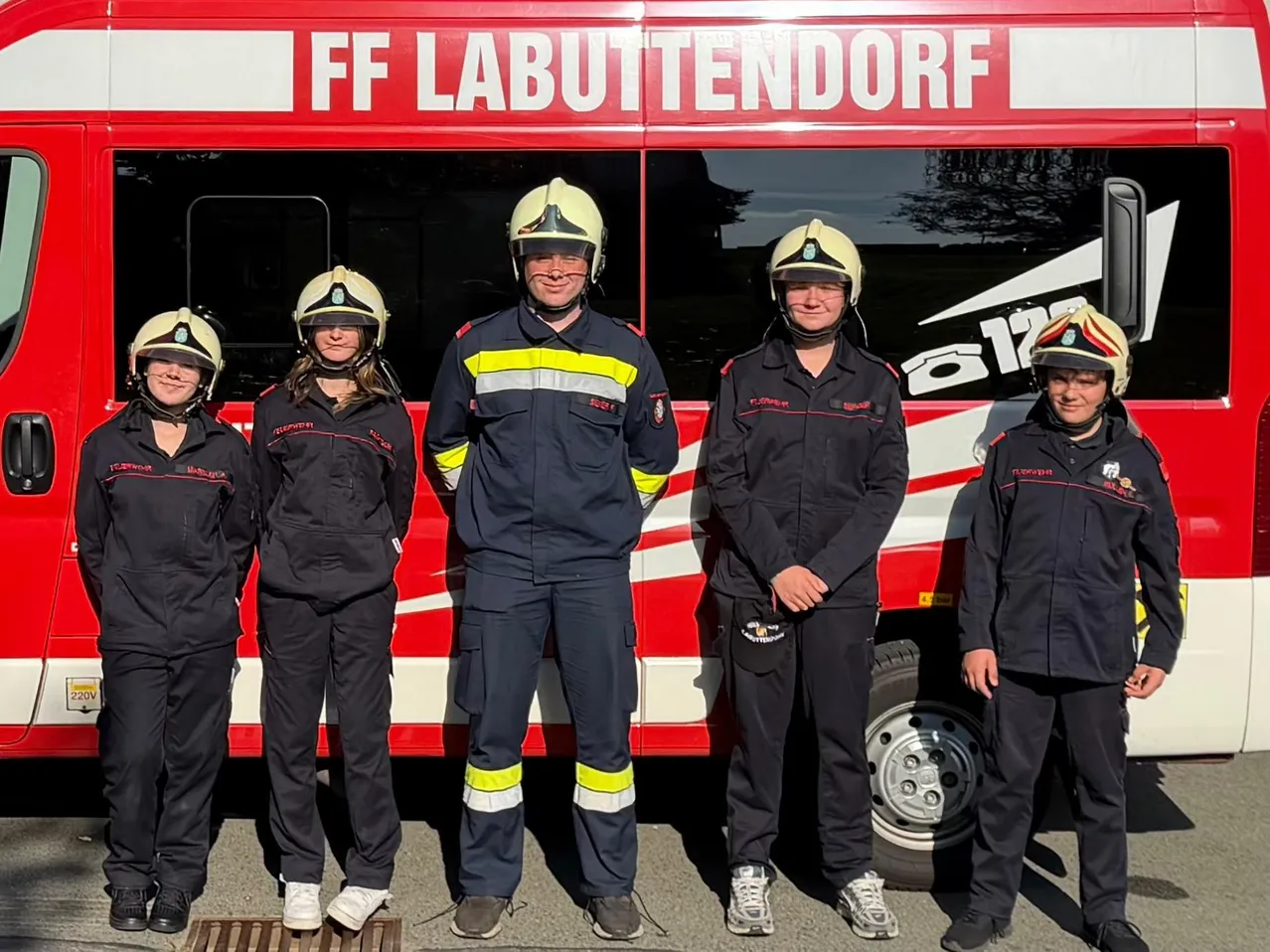 Fünf Personen in Feuerwehruniformen stehen vor einem roten Fahrzeug mit der Aufschrift FF Labuttendorf.