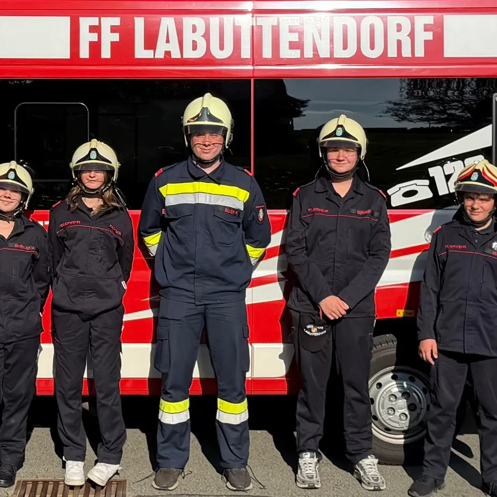 Fünf Personen in Feuerwehruniformen stehen vor einem roten Fahrzeug mit der Aufschrift FF Labuttendorf.