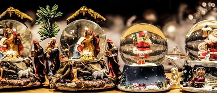 Auf einem Tisch sind verschiedene Feiertagsfiguren zu sehen, darunter eine Krippe und eine Schneekugel mit dem Weihnachtsmann und seiner Werkstatt.