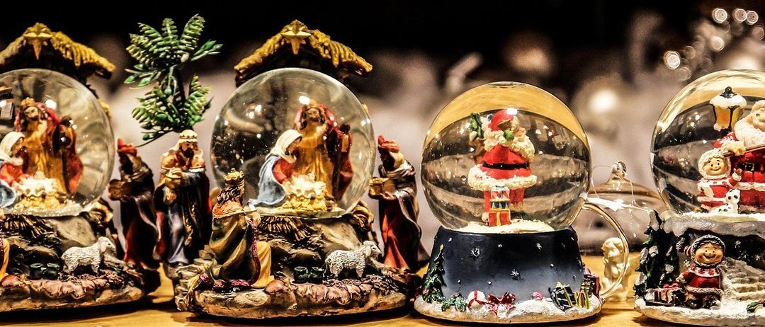 Auf einem Tisch sind verschiedene Feiertagsfiguren zu sehen, darunter eine Krippe und eine Schneekugel mit dem Weihnachtsmann und seiner Werkstatt.