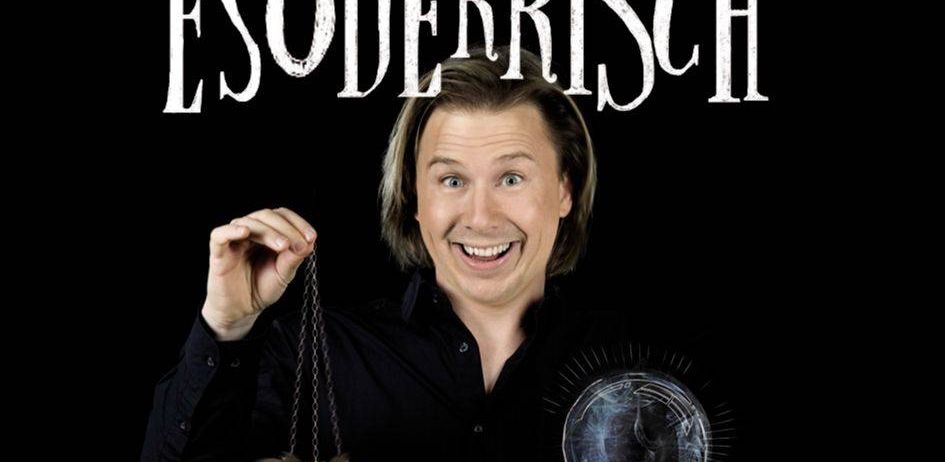 Ein Mann mit lächelndem Gesicht hält eine goldene Taschenuhr in einer Hand und eine Glaskugel in der anderen. Der Text 'ESODERRSCH' steht oben.