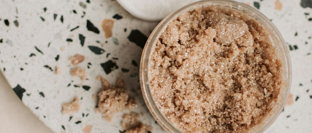 Ein Nahaufnahme einer weißen Marmoroberfläche mit einem Glas brauner Zuckerkörnchen, drei weißen runden Objekten und einem kleinen Stück Klebeband.
