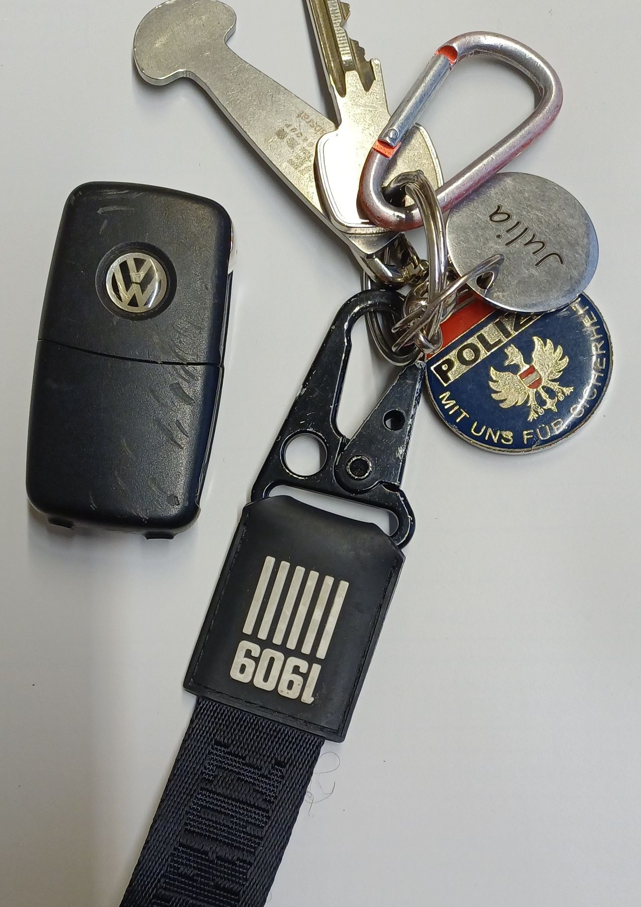 Ein schwarzer Volkswagen-Schlüsselanhänger, ein Schlüssel mit einem Lanyard mit der Aufschrift 6061 und ein Polizeiabzeichen mit dem deutschen Adleremblem.